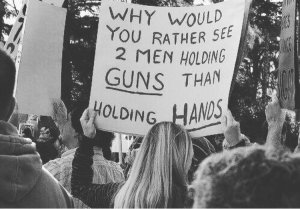 Sign reads, "Why would you rather see 2 men holding GUNS than holding HANDS."