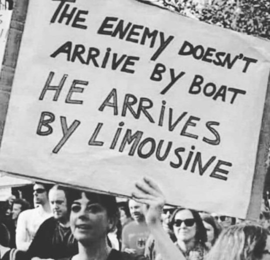 Historical photo of a woman at a protest holding up a sign that reads: “The enemy doesn't arrive by boat, he arrives by limousine.”