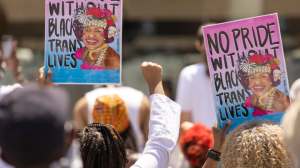 Two signs being held up in a crowd, each depicts Marsha P. Johnson, sports the Trans Pride Flag colors, and the phrase: “There would be no pride without black trans lives!”